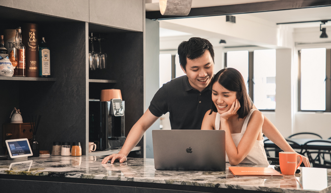 A young, Asian couple on the breakfast bar, looking at a laptop