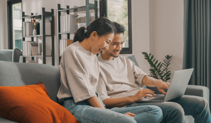Asian couple sitting on the couch, looking at a laptop