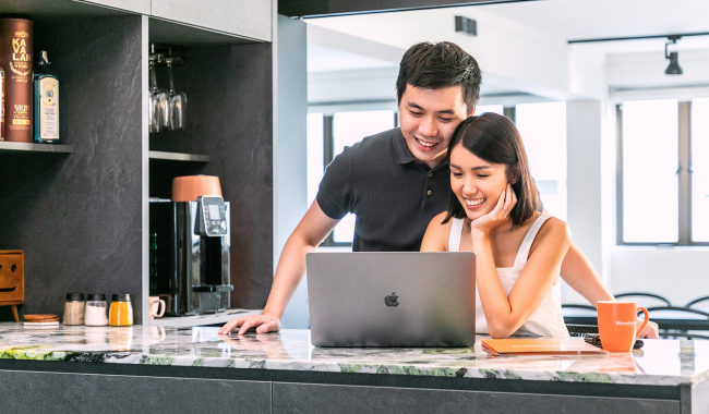 Asian couple on the breakfast bar looking at a laptop, smiling