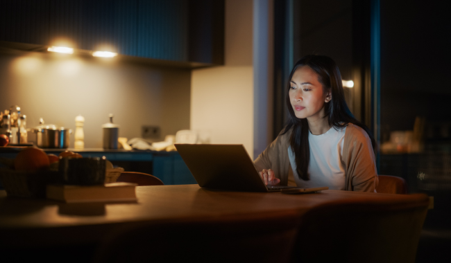 Asian woman at the dining table, scrolling on her laptop at night