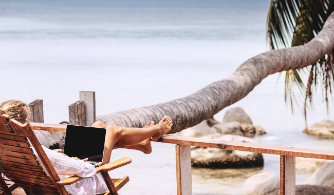 Woman on her laptop, lounging on a chair at a beach